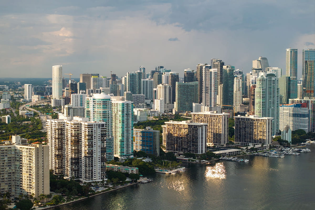 Aerial view of a waterfront city skyline with boats on the water under a partly cloudy sky.